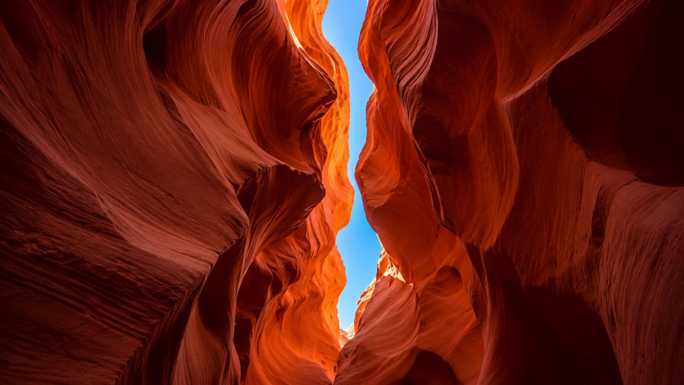 Looking straight up out of a narrow Antelope Canyon slot toward a thin ribbon of blue sky high above the sandstone walls