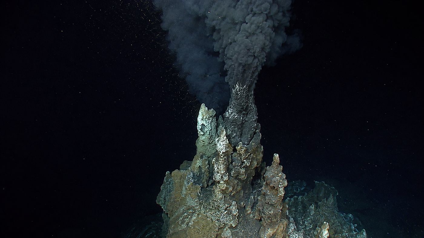 A black smoker hydrothermal vent chimney billowing dark mineral smoke into the deep sea