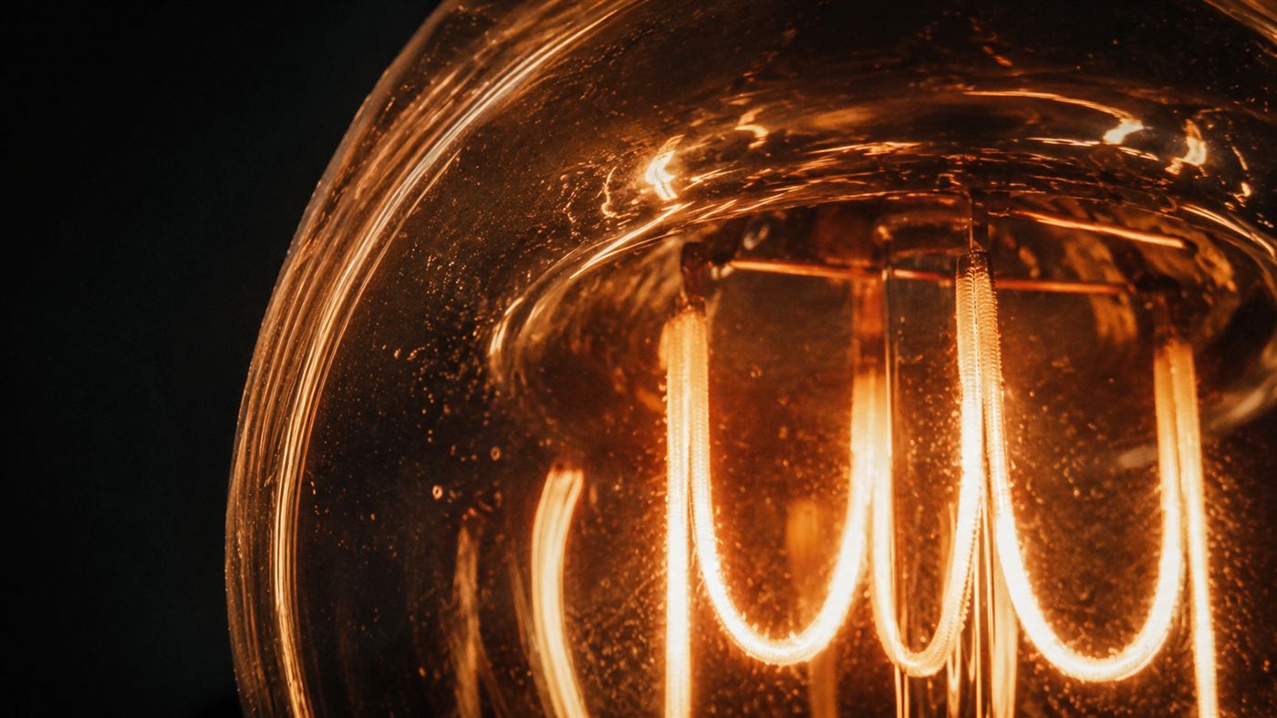 Extreme close-up of the thick glowing carbon filament inside an antique lightbulb, warm amber light against a dark background