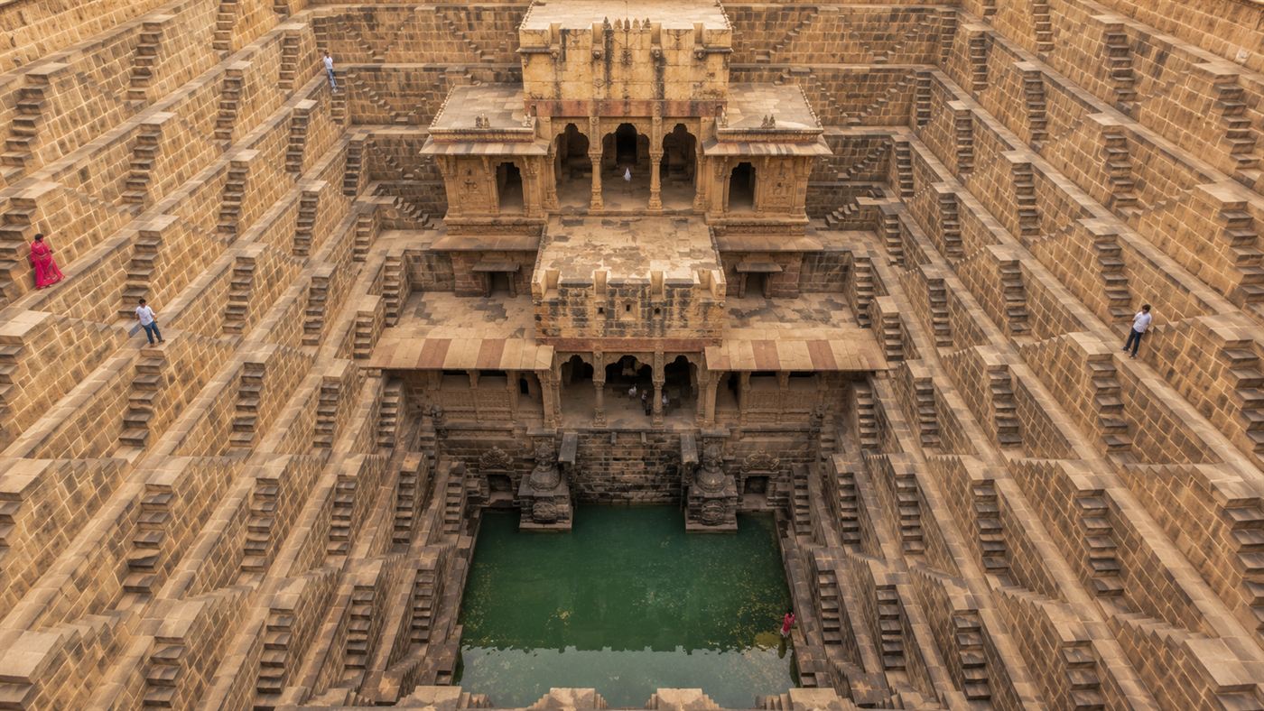 Looking down to the green water pool at the base of Chand Baori with the surrounding tiered galleries and a pillared pavilion on one side