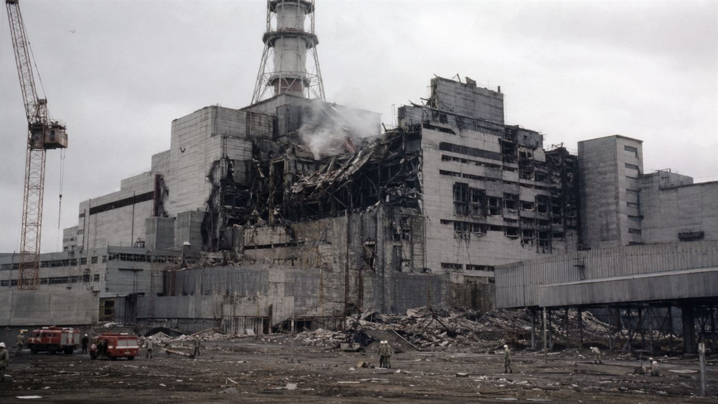 The damaged Chernobyl reactor building smoking in 1986 with workers and vehicles in the foreground