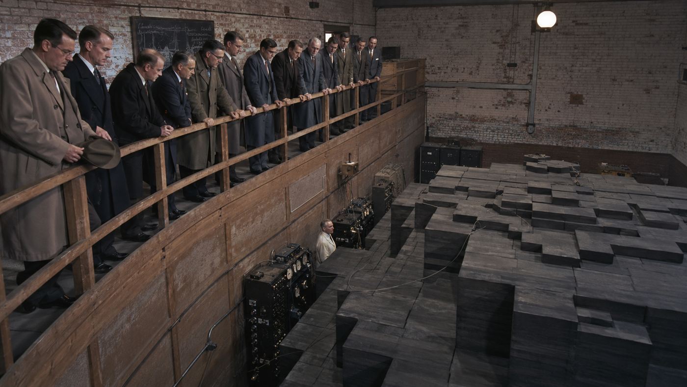 Scientists on a wooden balcony watching instruments above the dark graphite reactor of Chicago Pile-1, the first nuclear reactor