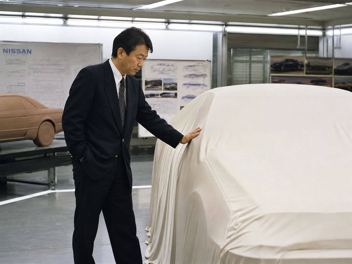 A chief engineer examining a car prototype in a 1990s studio, evoking Takeshi Uchiyamada and the Toyota Prius