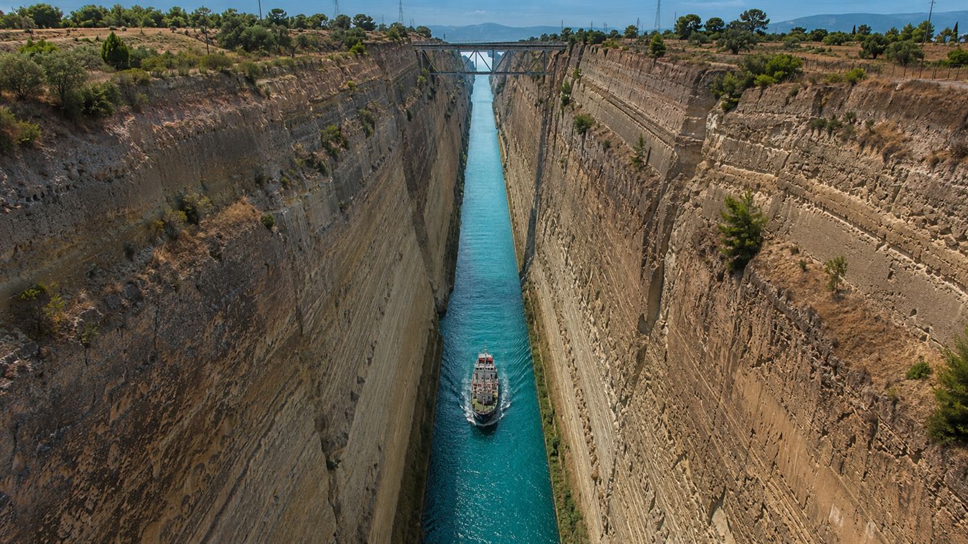 The narrow Corinth Canal cut deep between high vertical rock walls in Greece, a small ship passing through