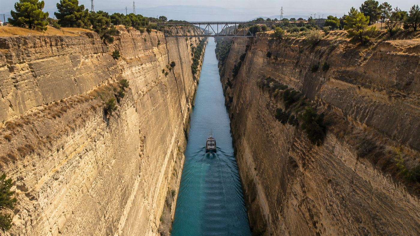 A small ship dwarfed by the towering vertical walls of the Corinth Canal as it passes through