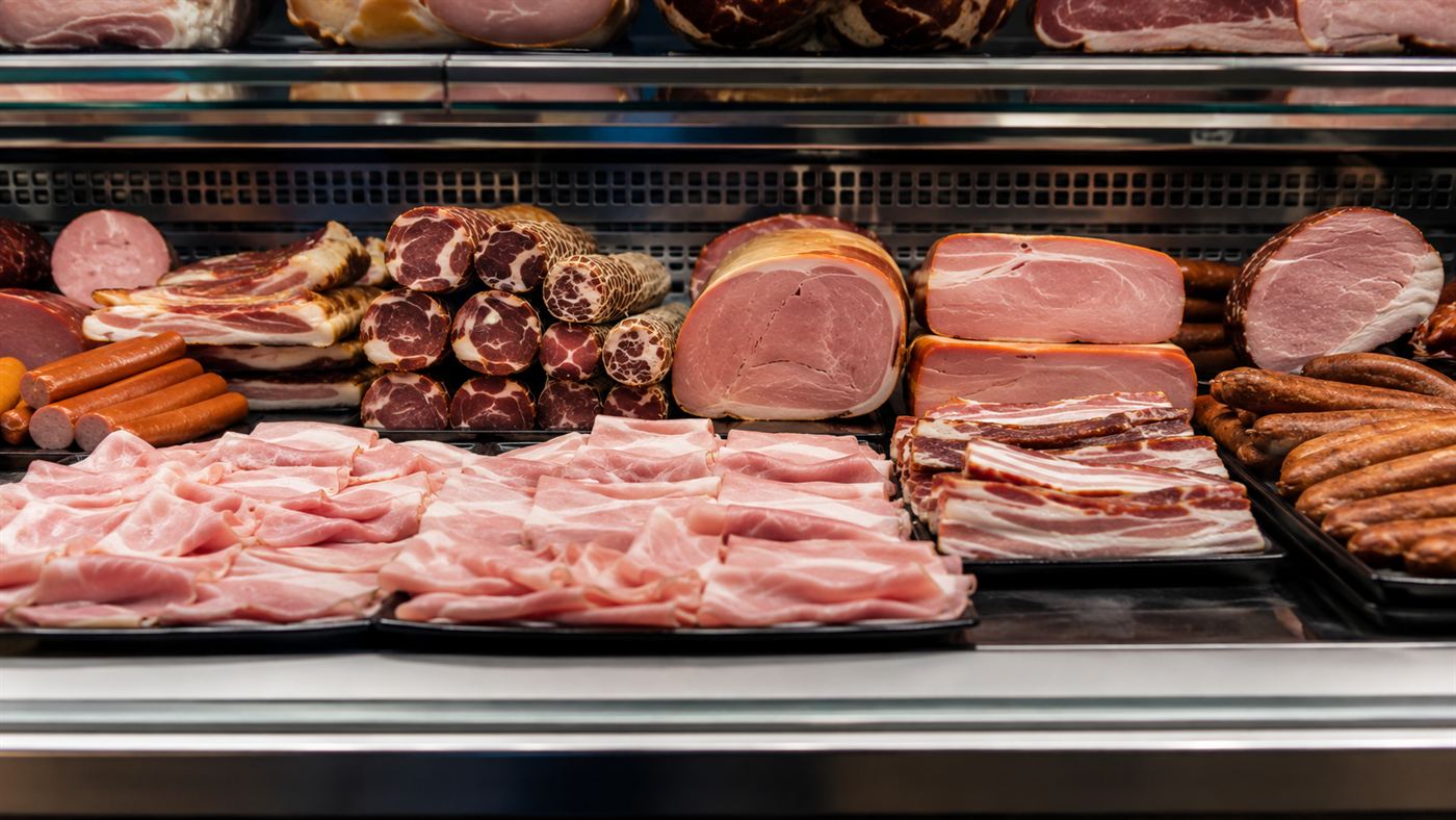 A deli counter display of cured and processed meats like ham, bacon and sausages