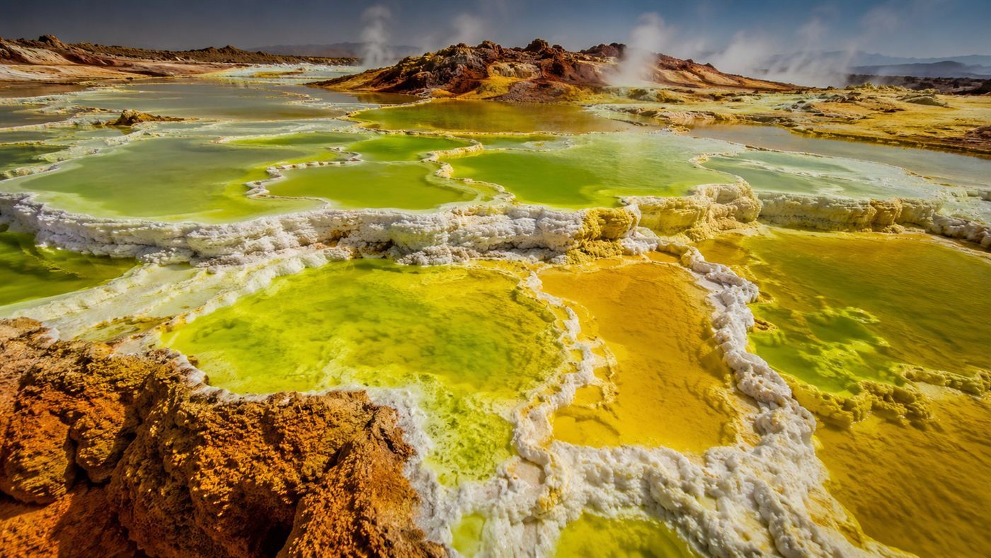 Surreal neon yellow and green acid pools with orange and white mineral crusts steaming in the Danakil Depression, an alien landscape