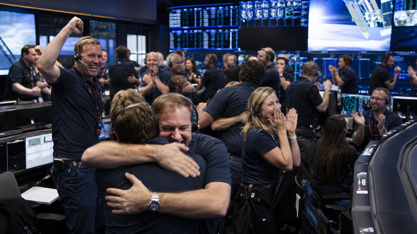 Scientists and engineers in a mission control room cheering after the successful DART asteroid deflection impact
