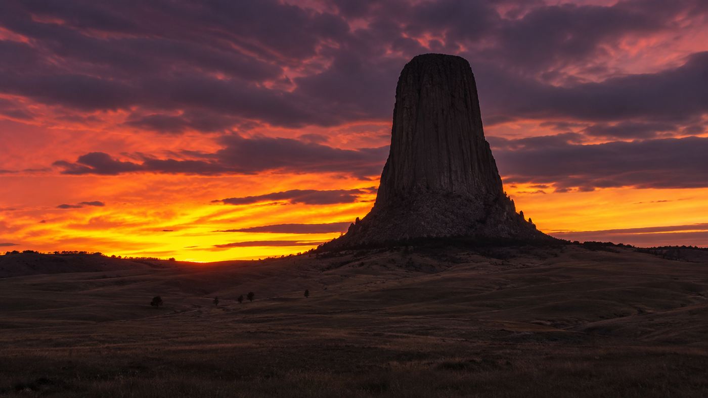 Devils Tower silhouetted against a glowing orange and purple sunset over the wide Wyoming plains