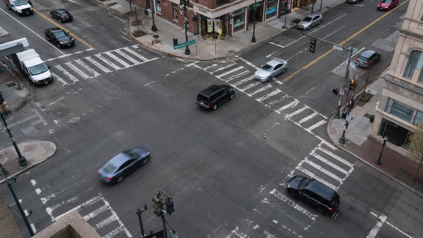 A busy downtown city intersection with worn asphalt and crosswalk lines seen from above