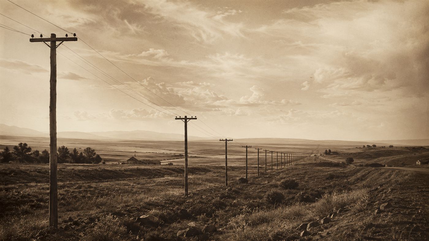 A line of wooden telegraph poles and wires stretching across the 19th-century American countryside toward the horizon