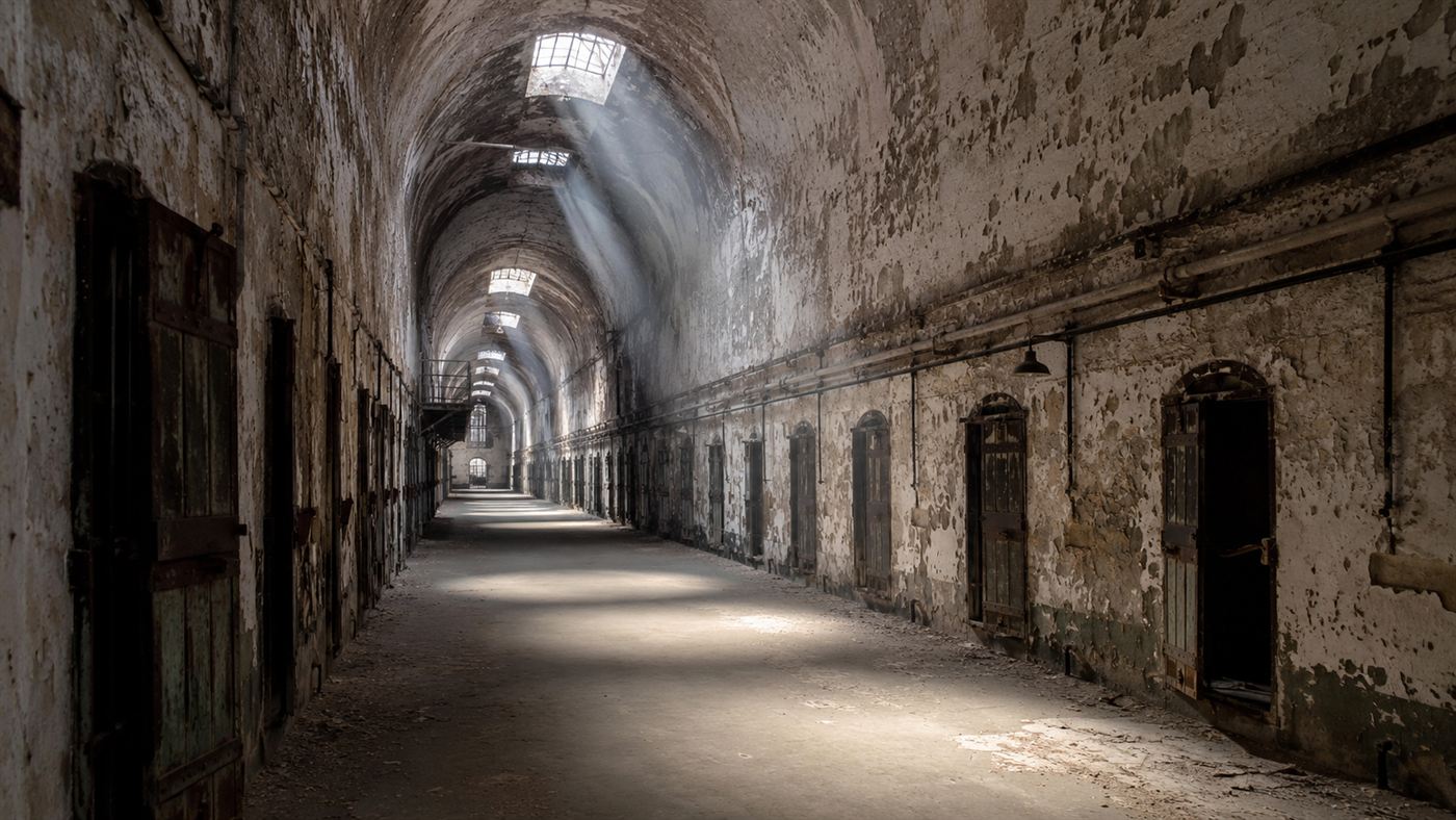 A long vaulted stone cell block corridor of Eastern State Penitentiary with rows of arched cell doors and light from skylights above