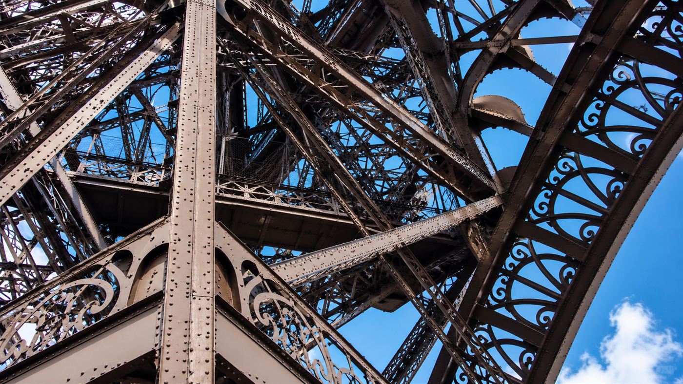 A close-up of the Eiffel Tower's wrought-iron lattice, showing the criss-crossing beams and rows of rivets