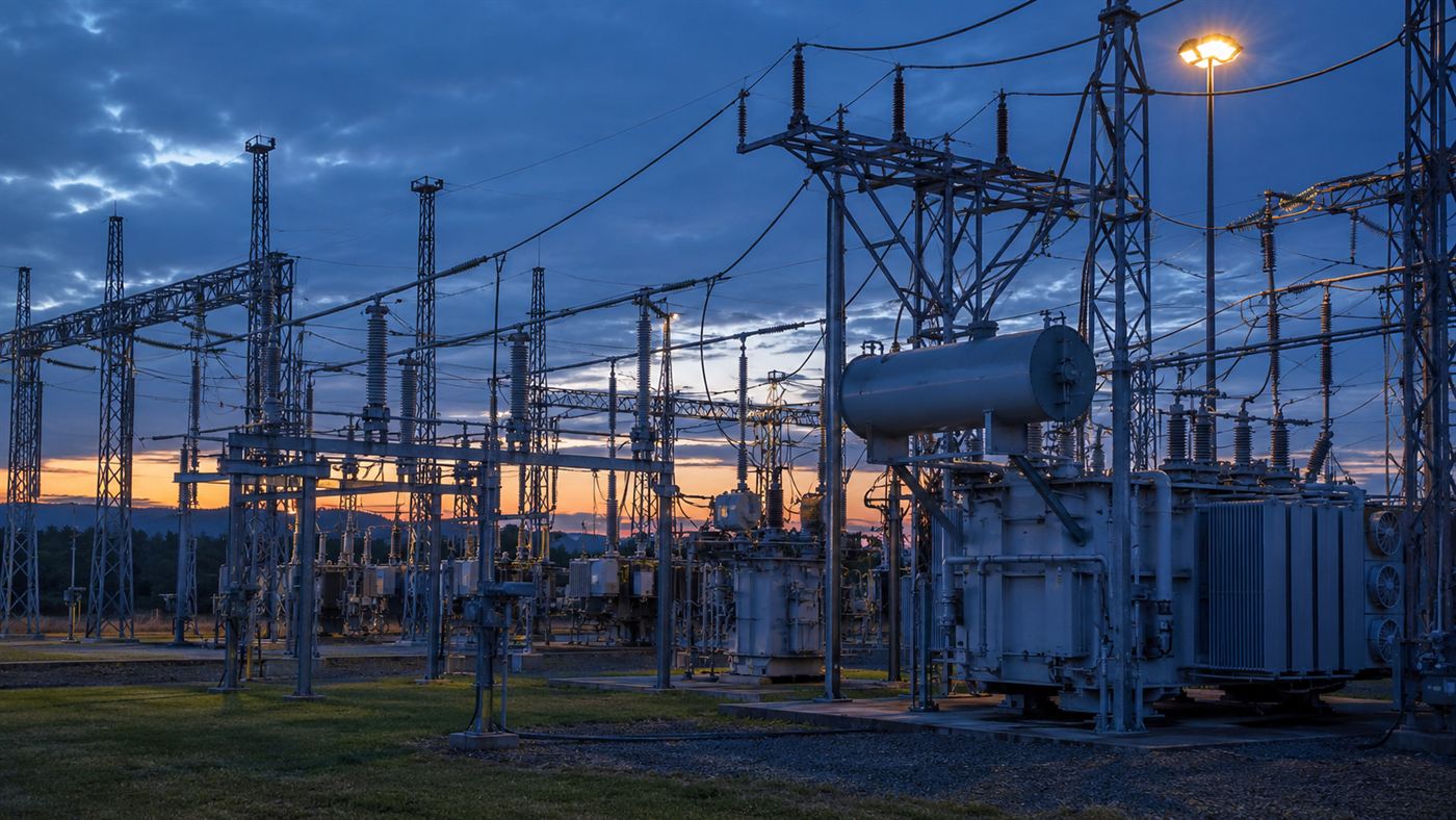 A large electrical substation full of transformers and wires at dusk, the kind of power grid equipment squirrels short out