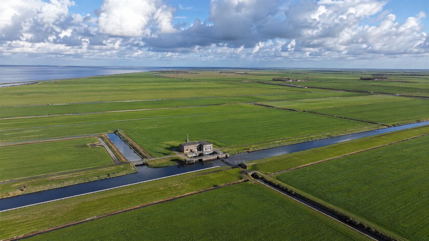 Flat reclaimed Dutch polder farmland with straight drainage canals and a pumping station, land that was once the seabed of the Zuiderzee