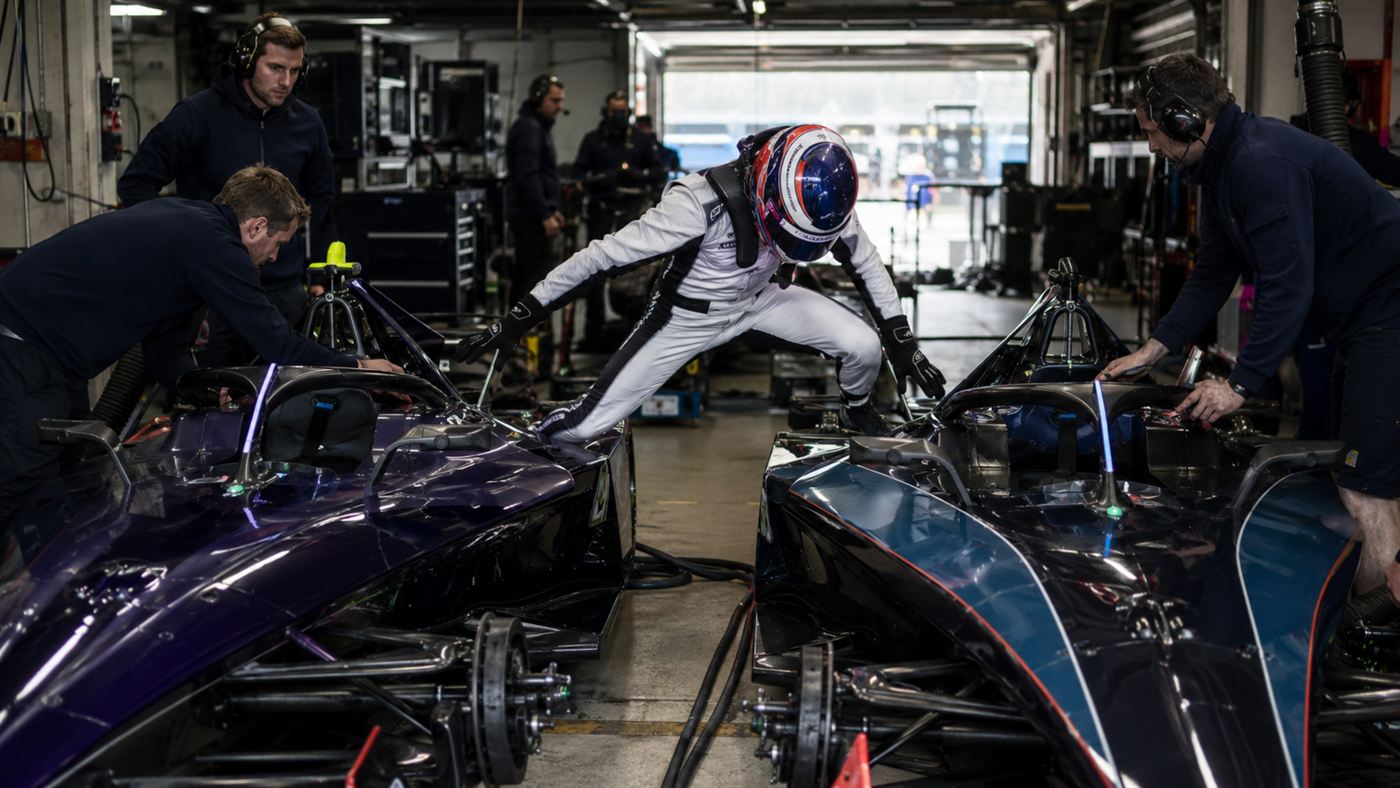 An early Formula E driver climbing from one electric car into a second fully charged one during a mid-race swap