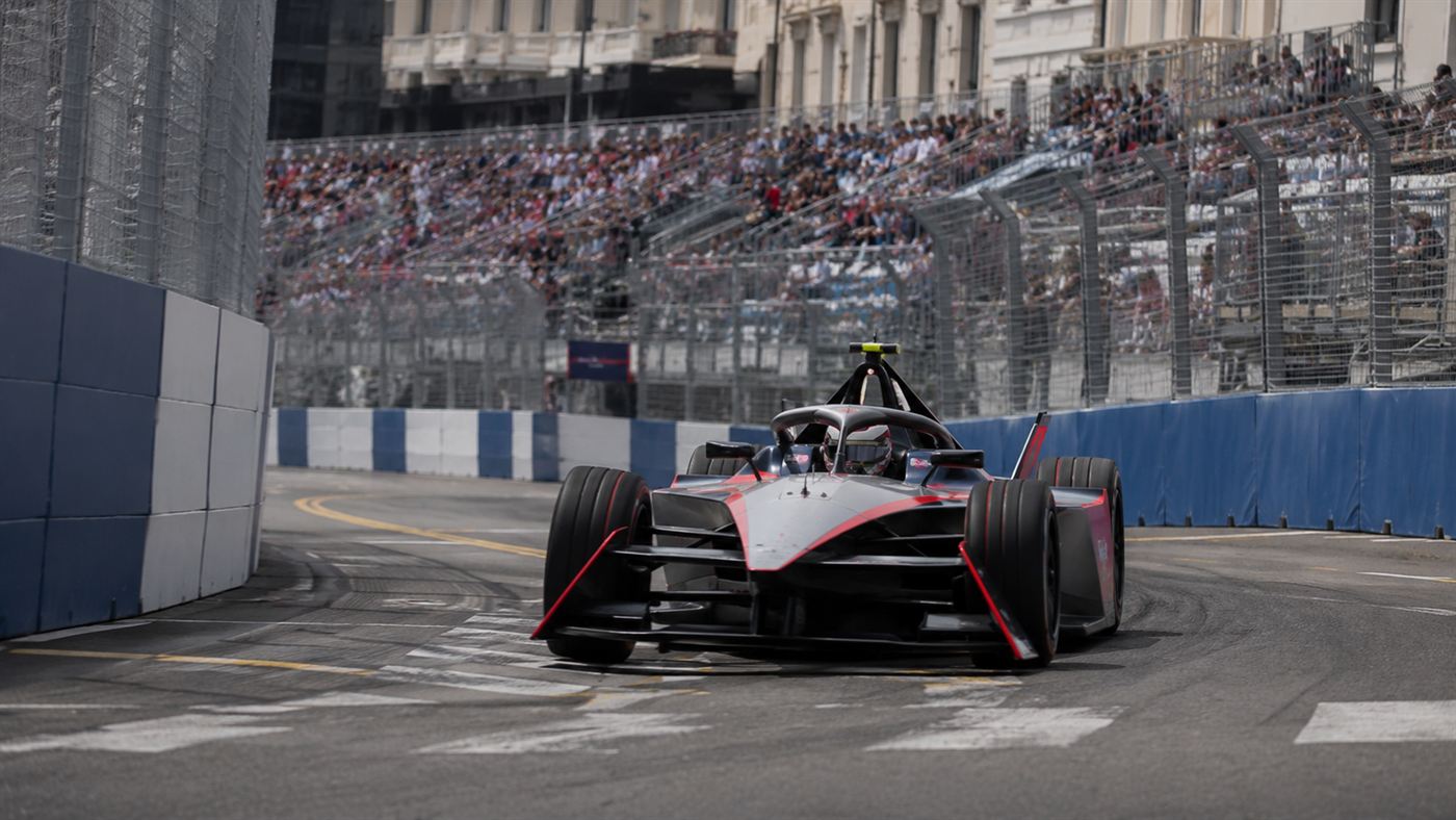 A Formula E electric single-seater racing car cornering on a city street circuit between barriers