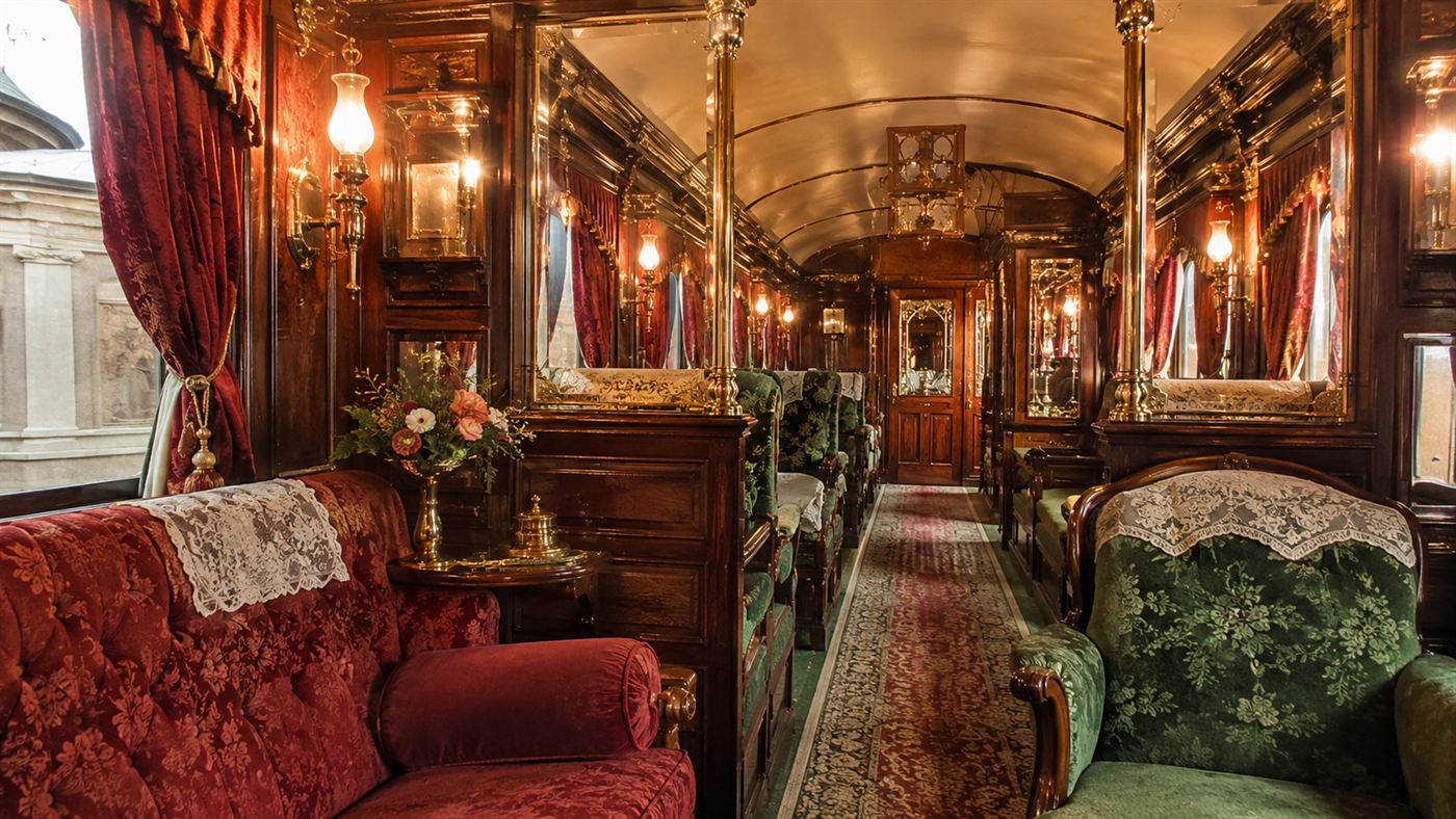 The ornate interior of a 19th-century Pullman Palace sleeping car with plush seats and woodwork