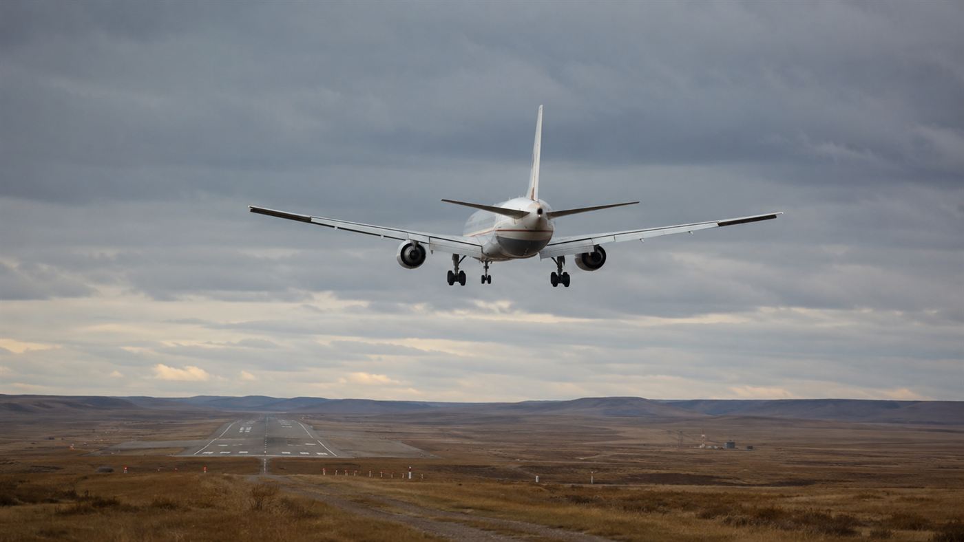 A white twin-engine airliner gliding silently toward a remote runway, the Gimli Glider making its powerless descent