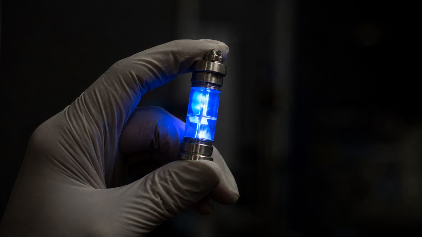 A gloved hand holding a sealed capsule glowing blue in the dark, evoking the Goiânia accident cesium source