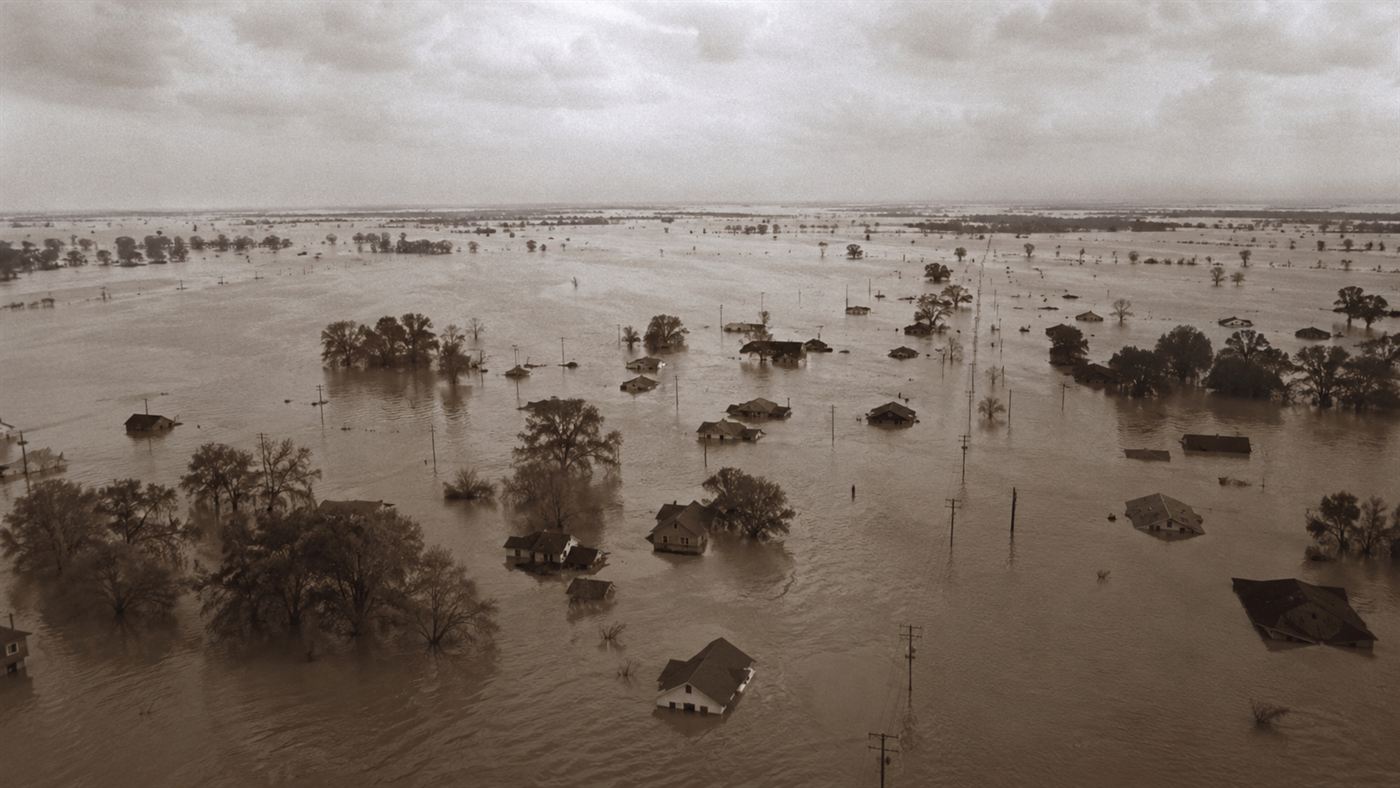 Floodwater from the Great Mississippi Flood of 1927 swallowing a Southern town, rooftops and trees rising from a brown inland sea