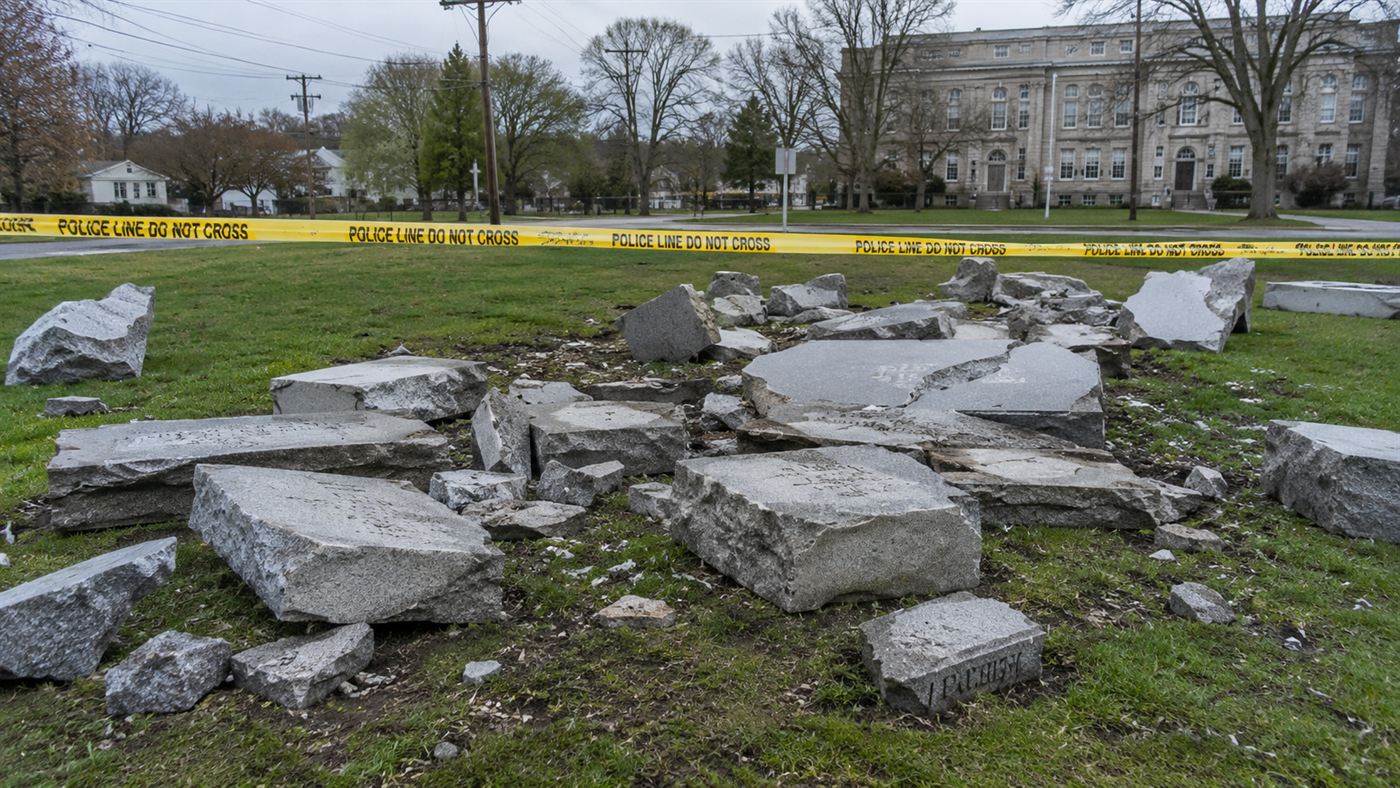 Shattered slabs of grey granite from the Georgia Guidestones lying toppled on the grass behind police tape