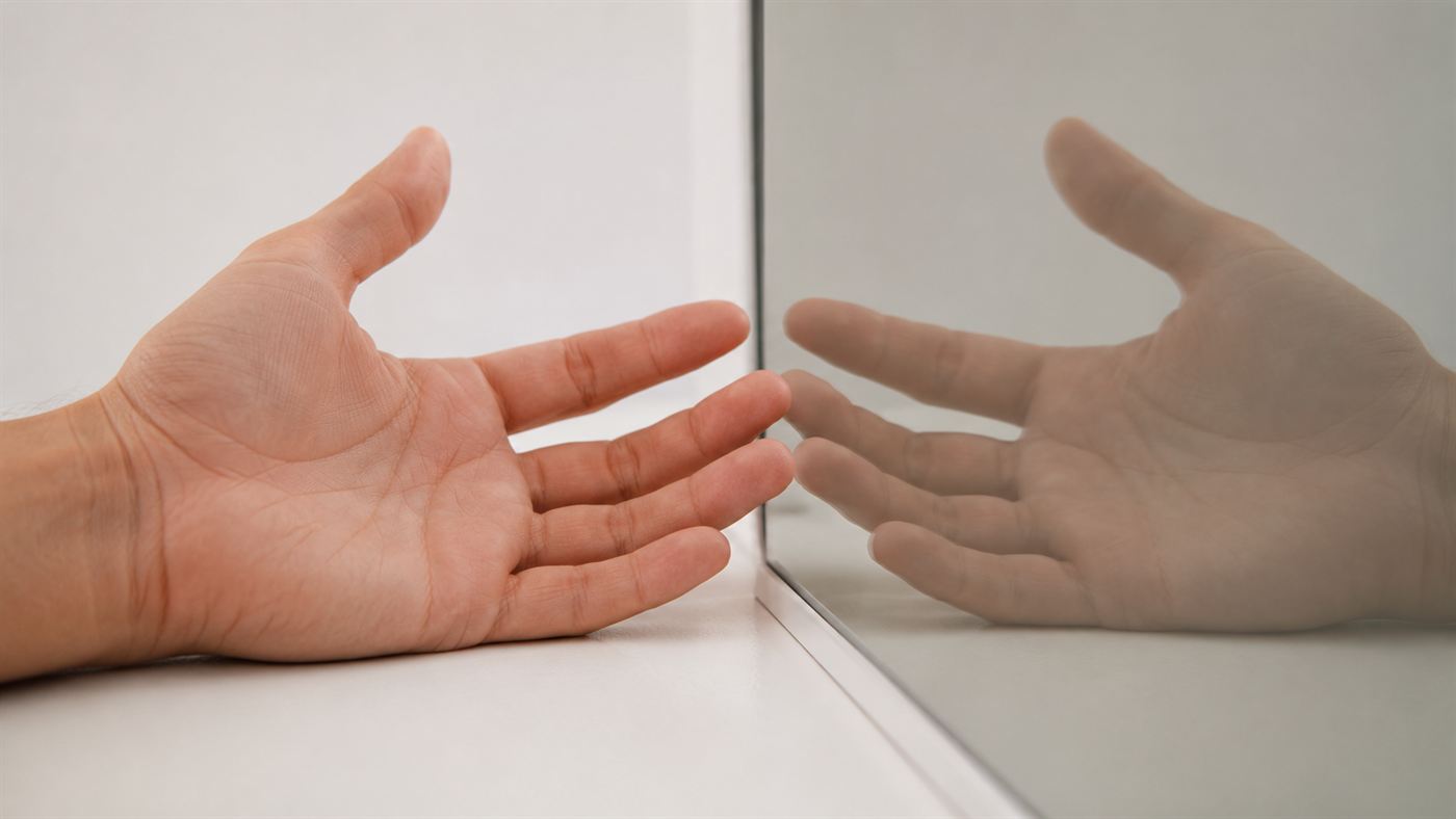 A single open hand resting beside a mirror that reflects it, creating the illusion of two hands