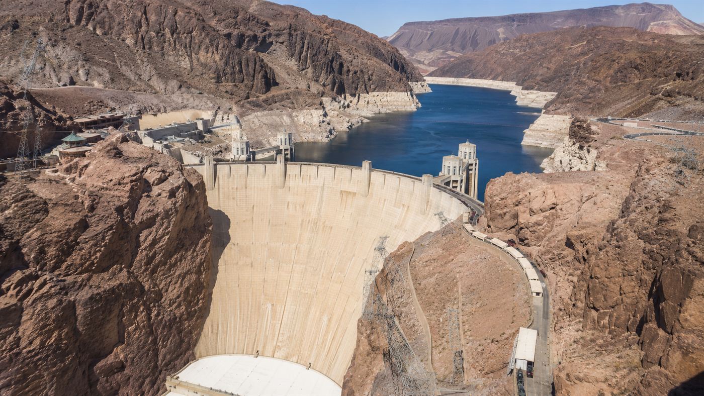 The Hoover Dam, a huge curved concrete dam wedged in a desert canyon holding back a blue reservoir