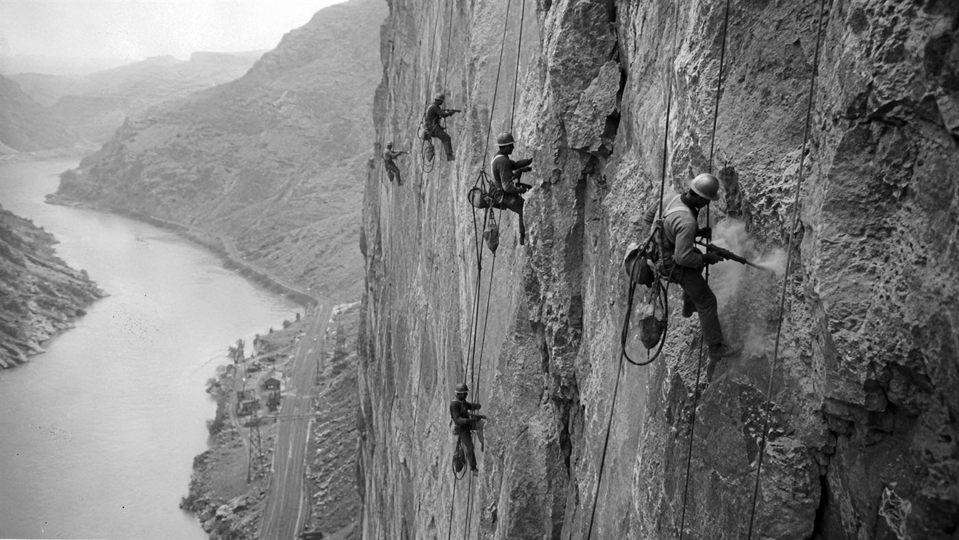 High scaler workers dangling on ropes down a sheer canyon wall during Hoover Dam construction