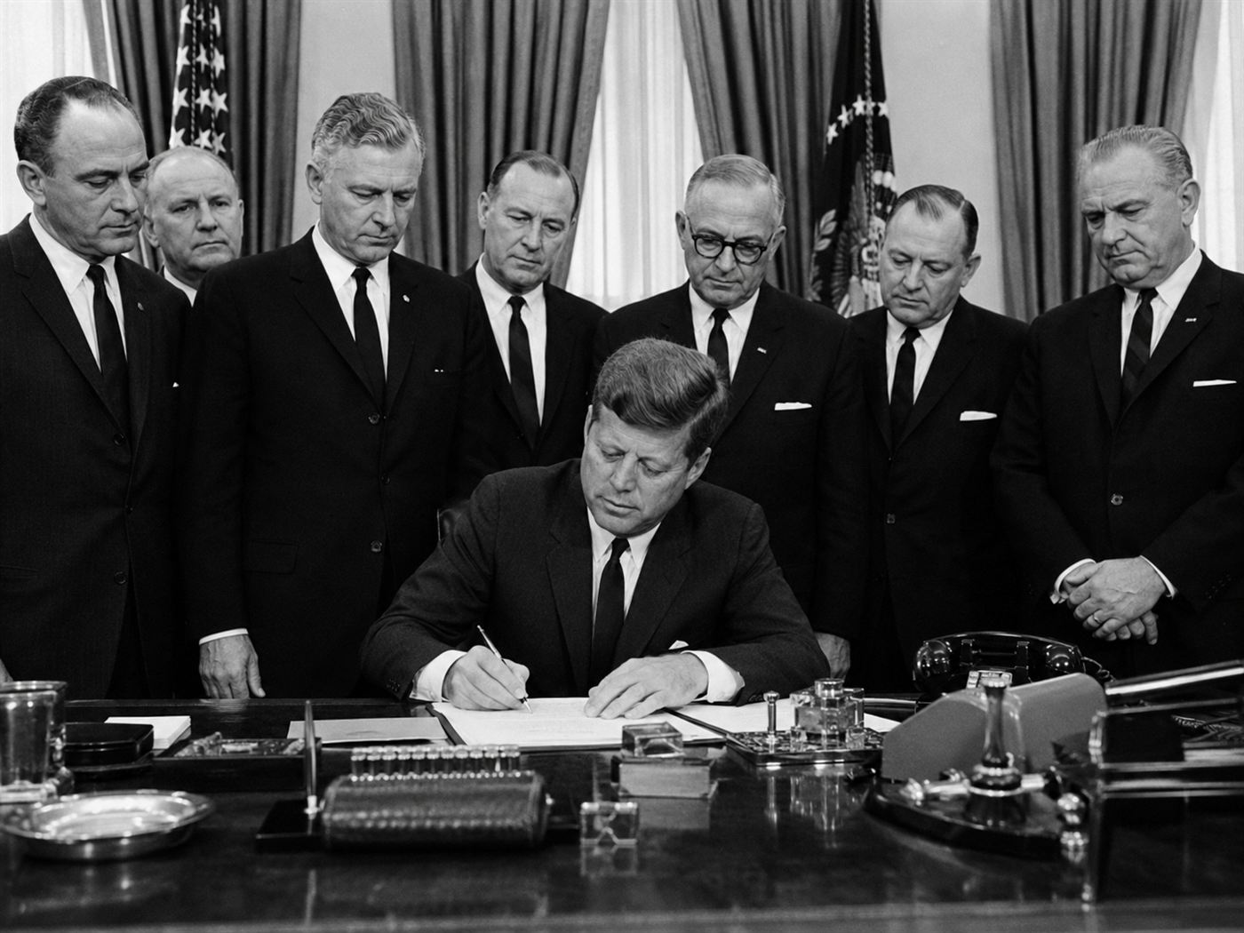 President John F Kennedy signing the Kefauver-Harris Drug Amendments of 1962 in the White House surrounded by members of Congress and FDA officials in dark suits
