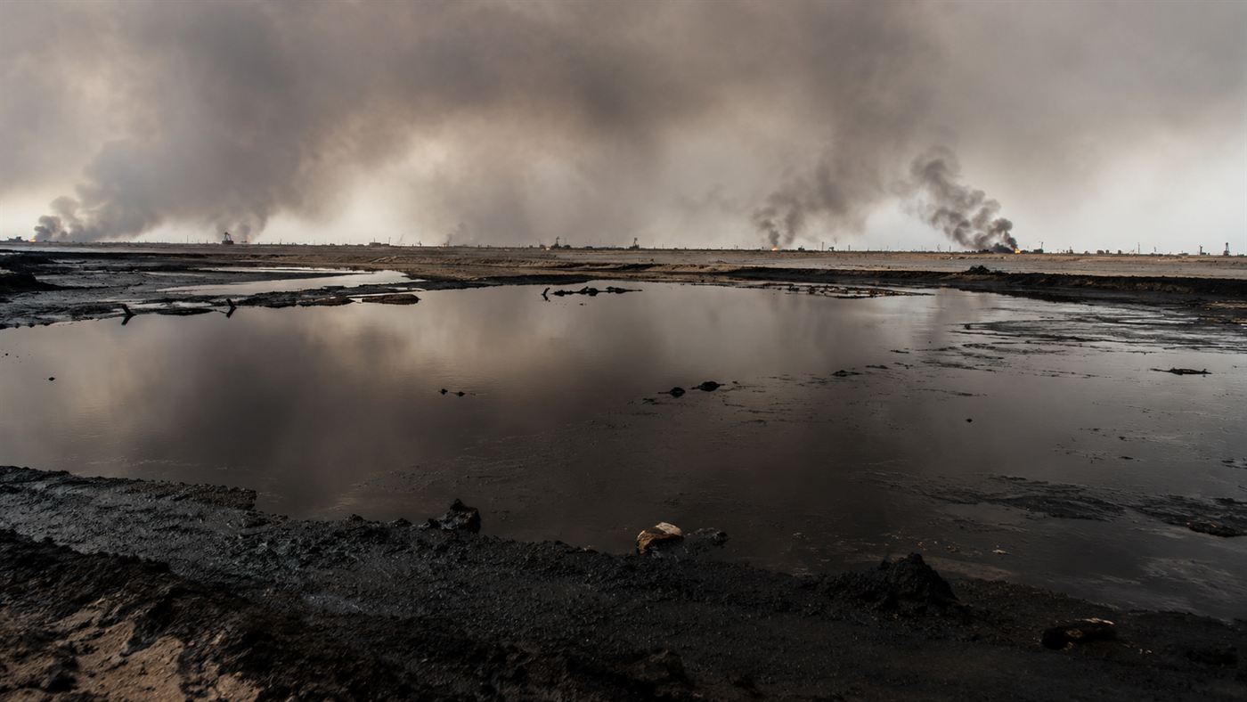 A black lake of spilled crude oil in the Kuwaiti desert under a smoke-darkened sky