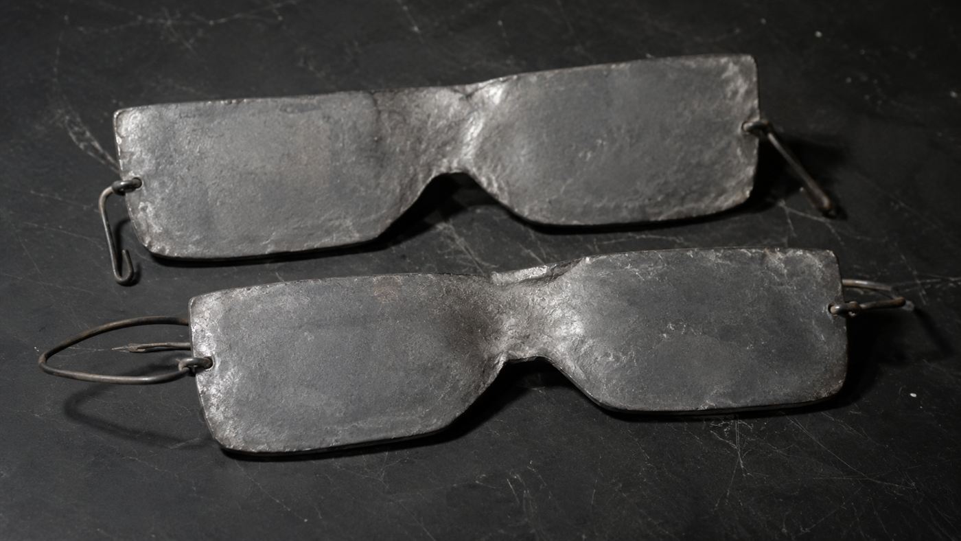 Two crude rectangular lead eye masks lying on a dark surface as forensic evidence