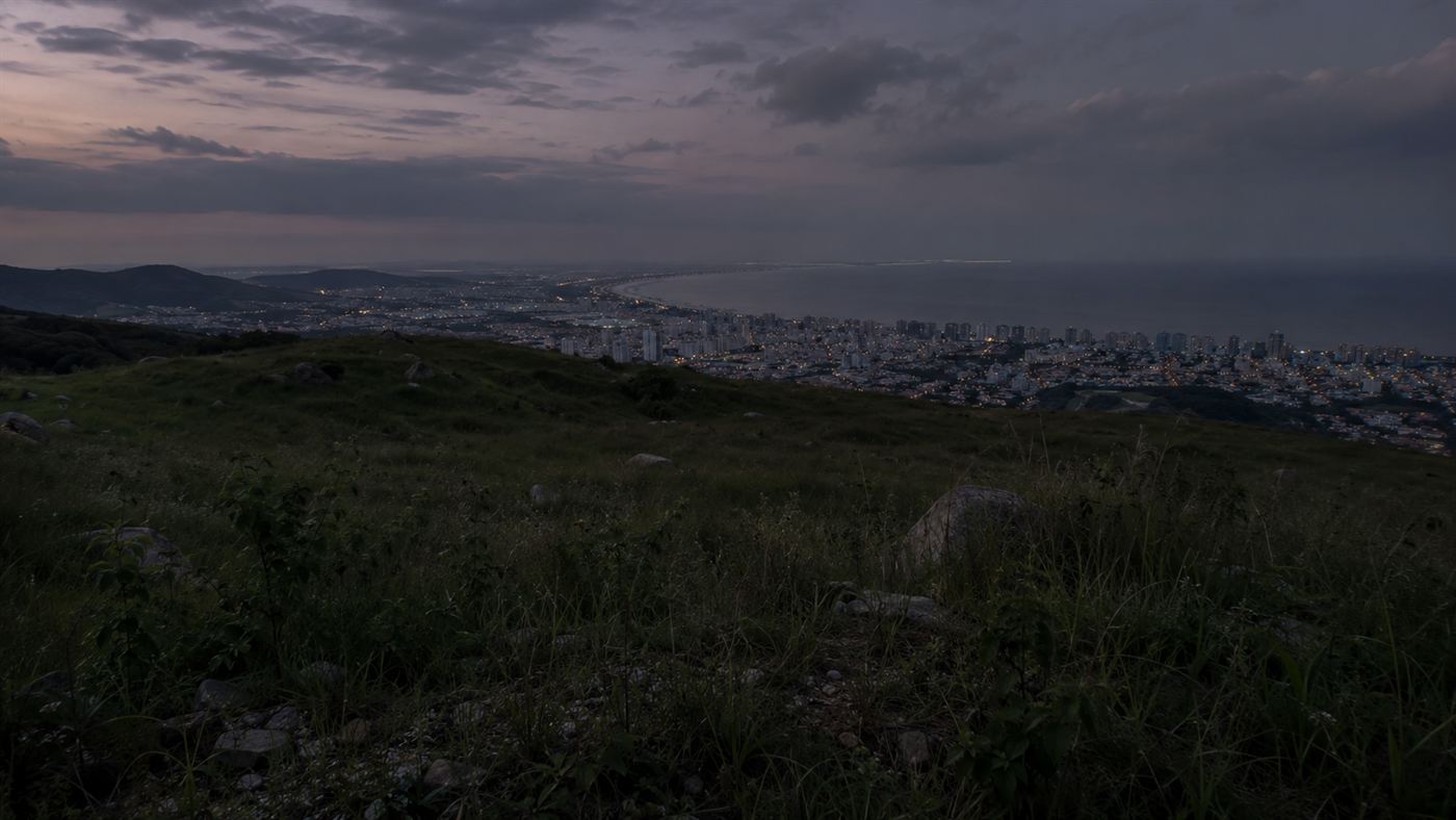 A lonely grassy hilltop overlooking a Brazilian coastal city at dusk, the setting of the Lead Masks Case