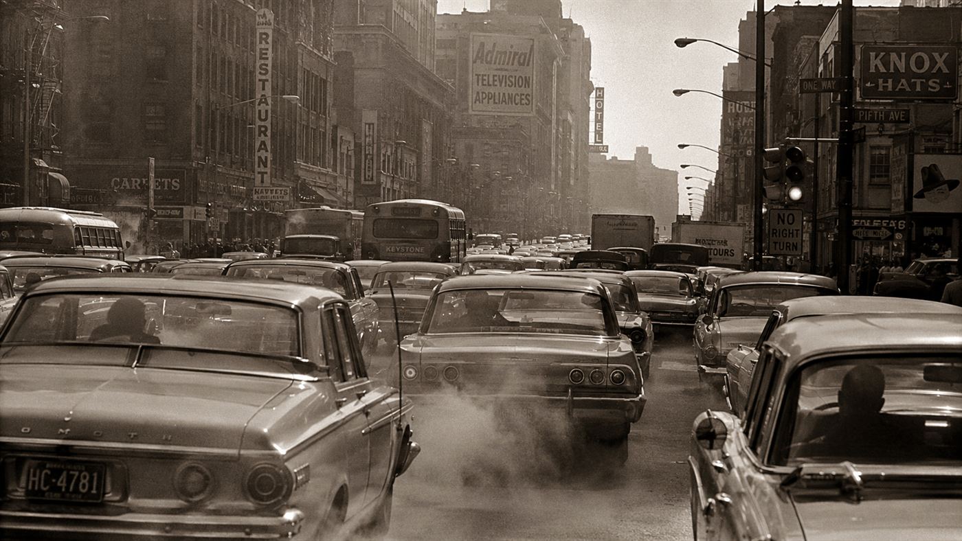 Heavy 1960s city traffic pouring exhaust into a smoggy street, the era of leaded petrol