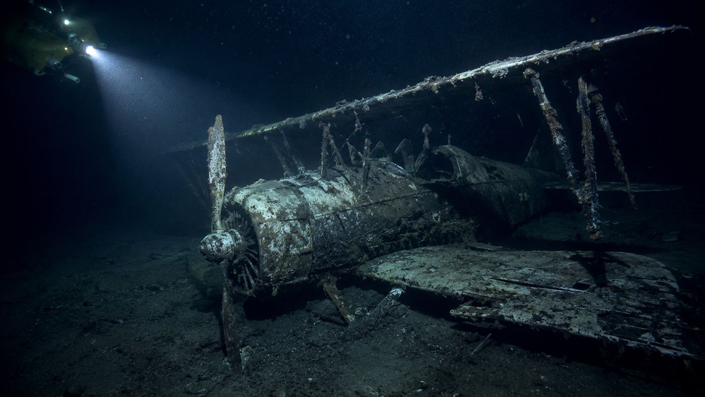 The remains of a biplane fighter resting on a dark seafloor, part of a sunken airship wreck site