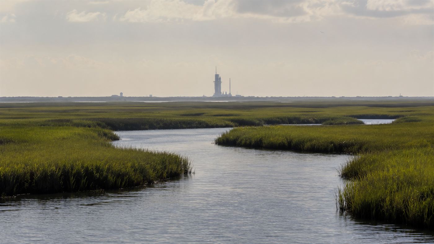 A wide Florida salt marsh of cordgrass with a distant rocket launch tower on the horizon