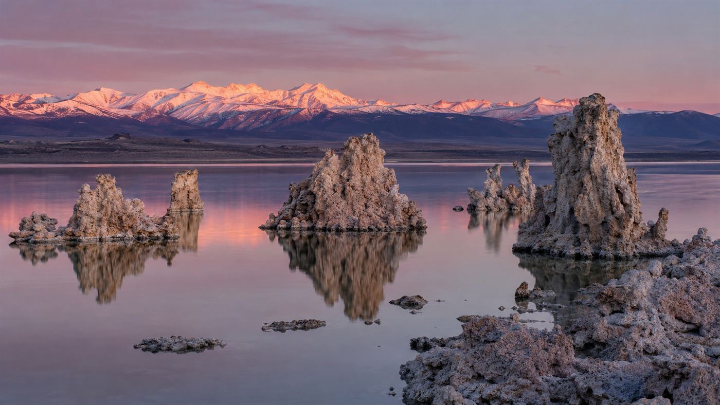The eerie tufa towers of Mono Lake, California rising from still water at sunrise with the Sierra Nevada behind