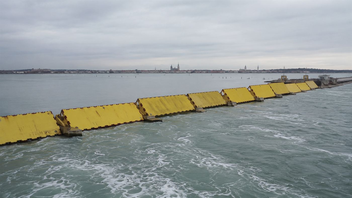 Yellow MOSE flood barrier gates raised out of the water at a Venice lagoon inlet, holding back the sea