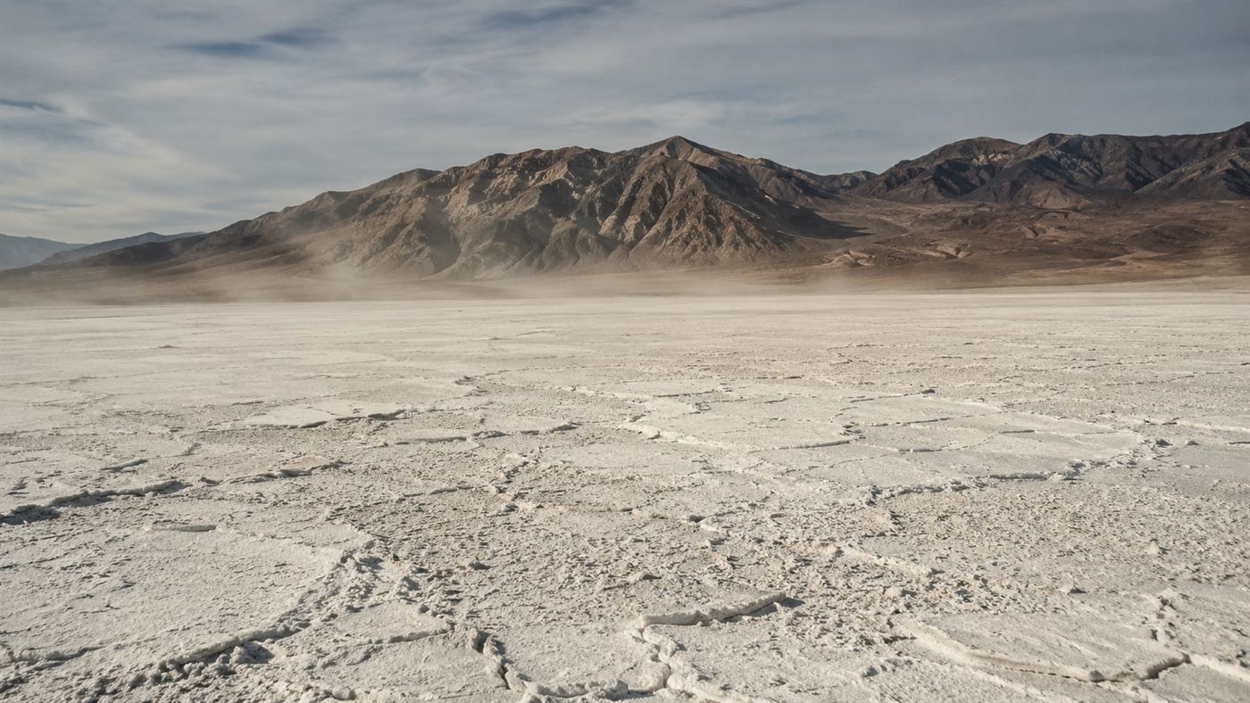 The cracked white salt flat of the dried Owens Lake bed stretching toward mountains under a dusty sky