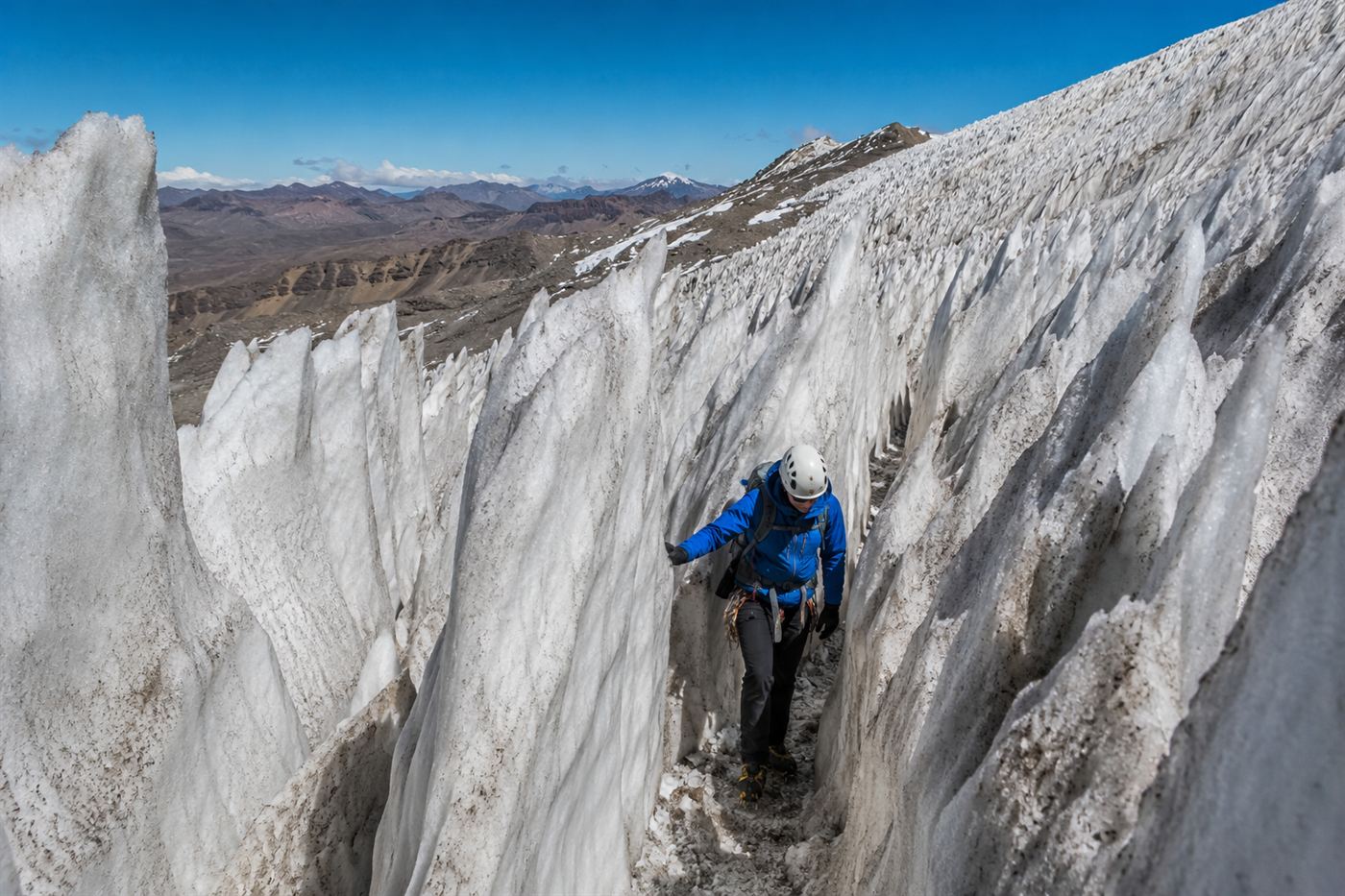 A climber threading a narrow path through a dense field of tall sharp ice penitentes leaning toward the sun on a high Andean slope