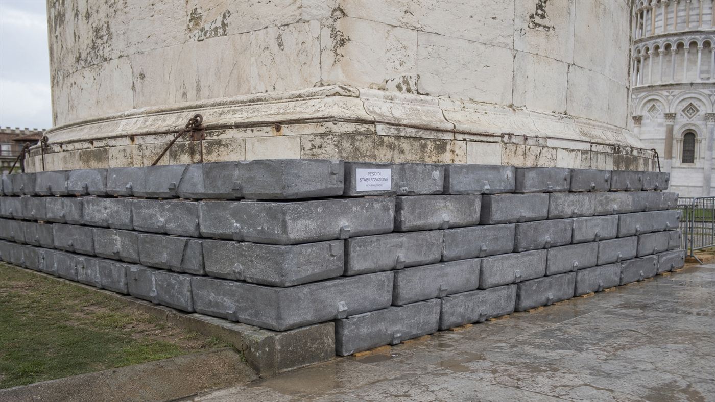 Stacked grey lead counterweight ingots arranged against the base of the leaning tower