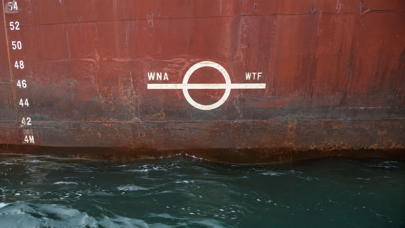 Close-up of a ship's steel hull at the waterline showing the round Plimsoll load line marking painted in white