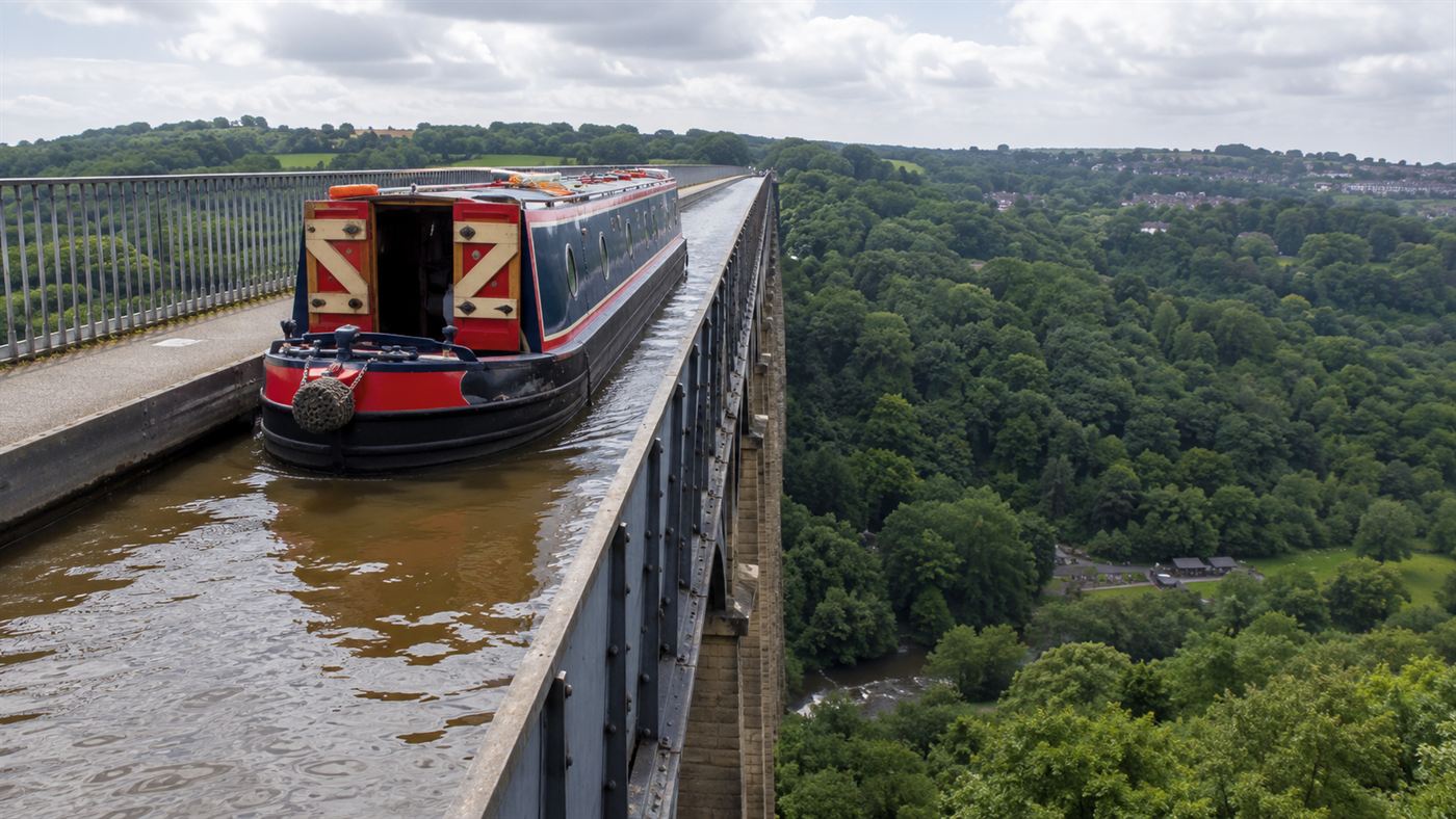 A narrowboat crossing the Pontcysyllte Aqueduct with a railed towpath on one side and a sheer open drop on the other