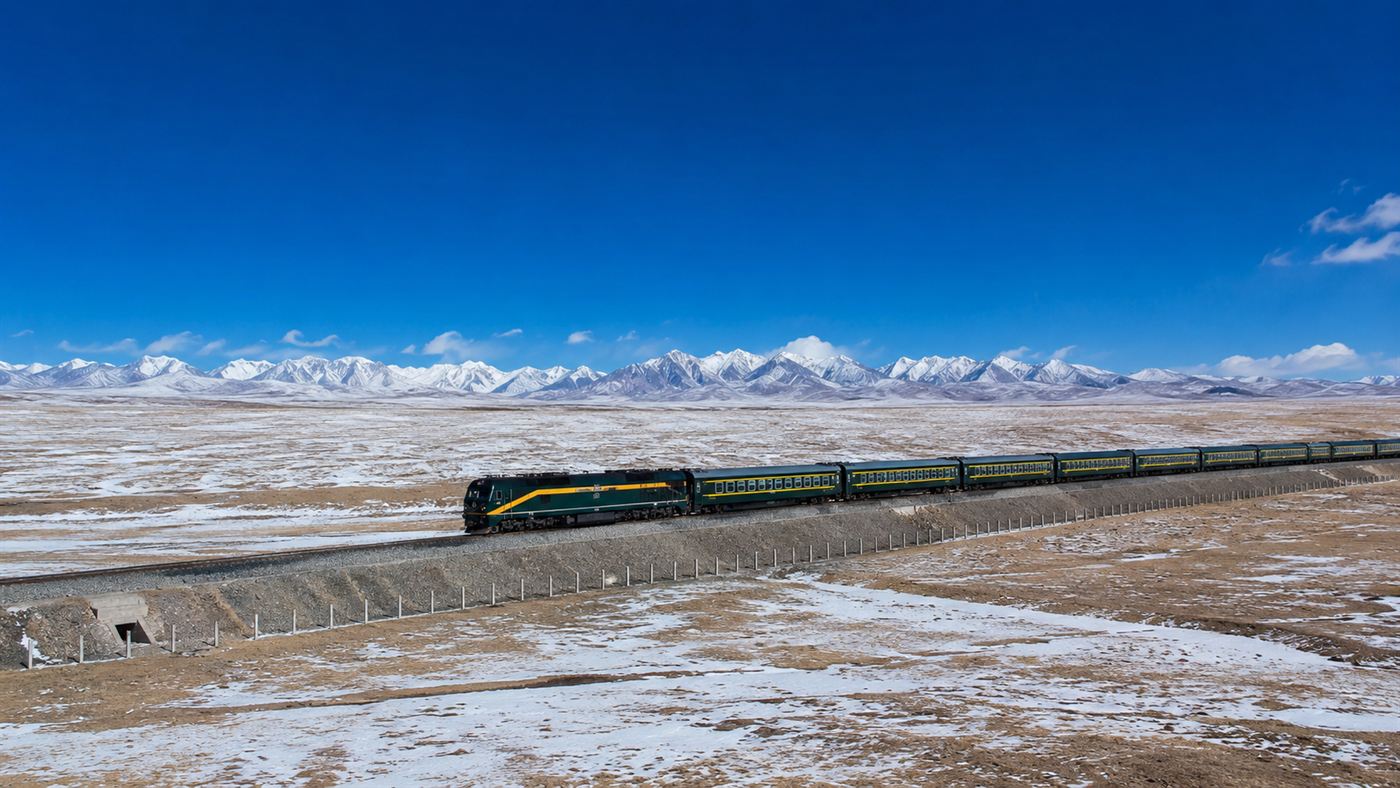 A train on the Qinghai-Tibet Railway crossing a vast high plateau with snow-capped mountains