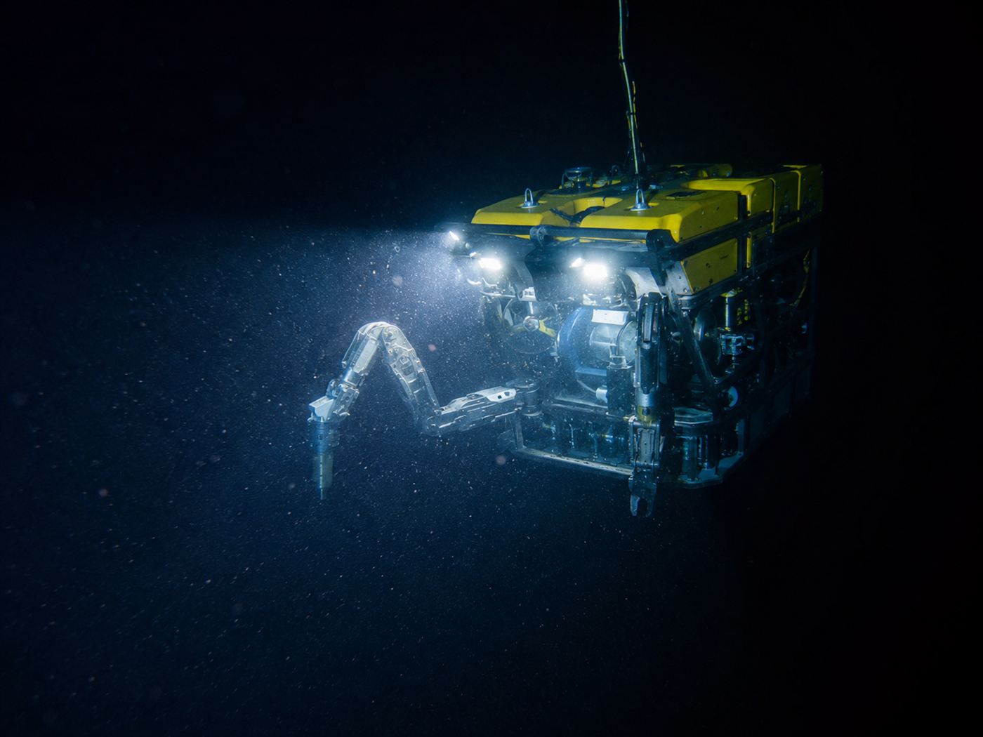 A remotely operated underwater robot with bright lights and mechanical arms exploring the dark deep sea