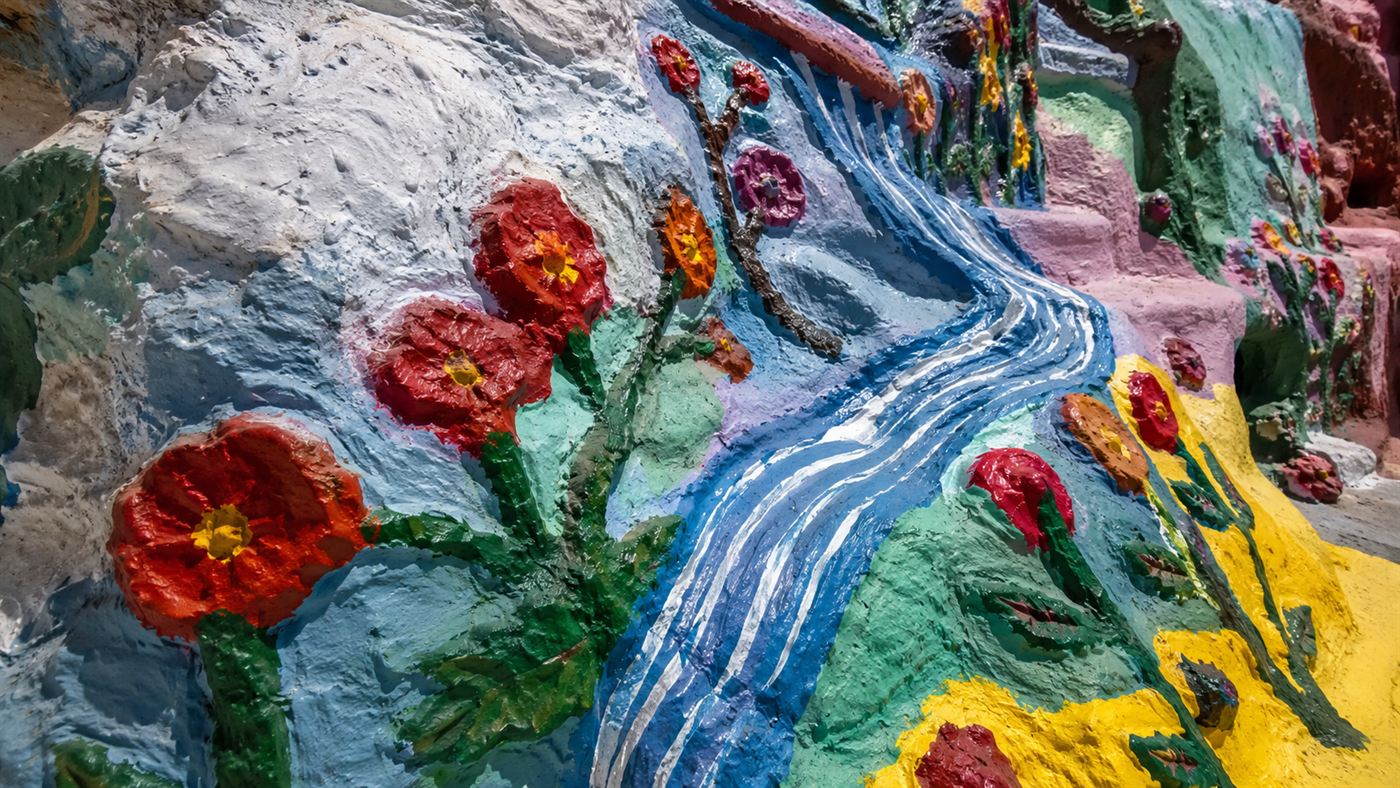 A close view of the thickly layered bright latex paint on Salvation Mountain, painted flowers and streams over sculpted adobe