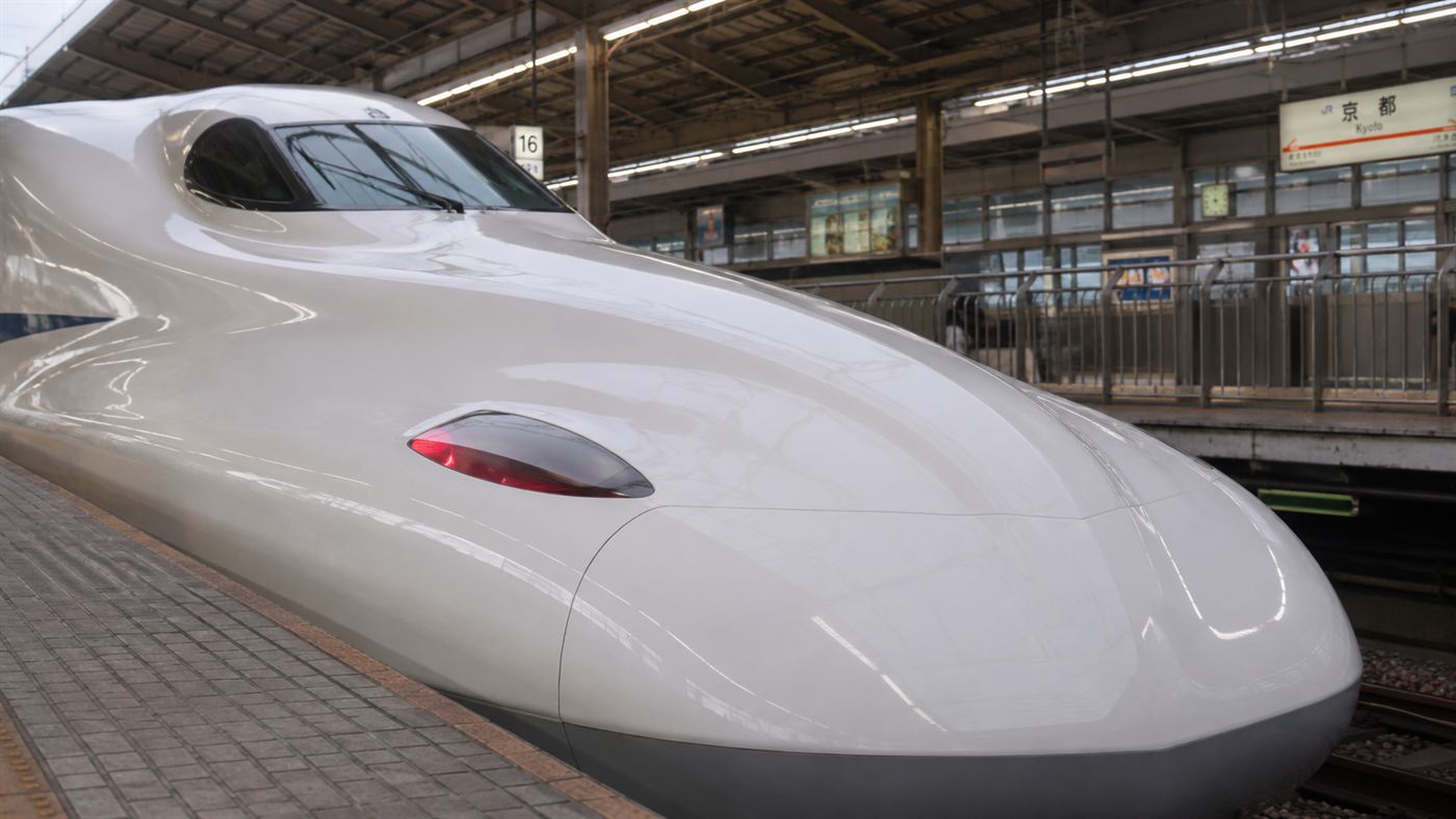 Close-up of the long aerodynamic nose of a modern white Shinkansen bullet train at a Japanese station platform