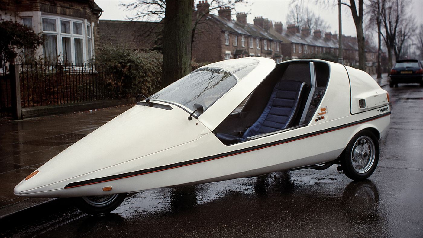A white single-seat Sinclair C5 electric trike with a long nose, parked low on a grey British street