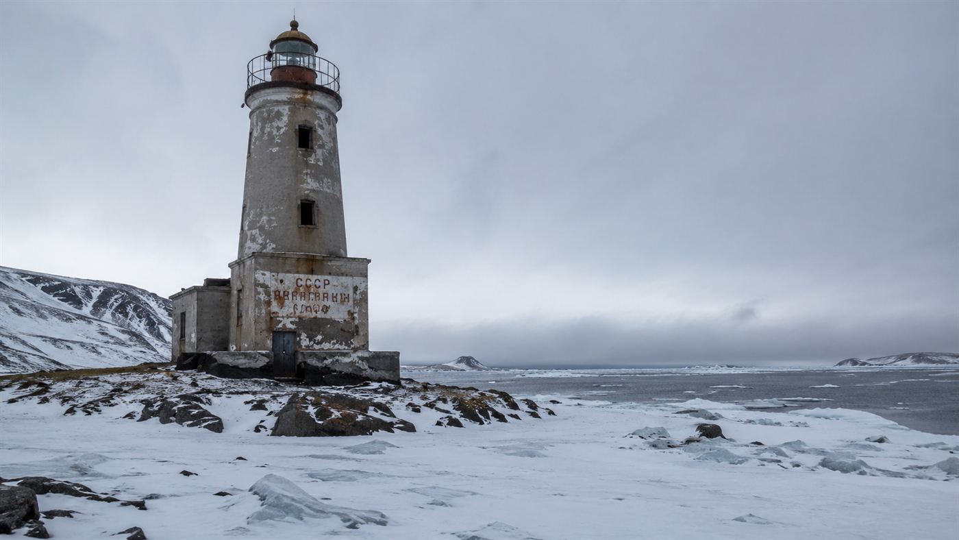 A lonely abandoned concrete lighthouse on a frozen Arctic coast under a grey sky, a Soviet nuclear lighthouse