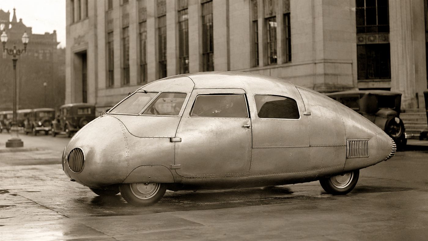 The 1936 Stout Scarab, a rounded streamlined beetle-shaped car with smooth metal bodywork, parked on a street